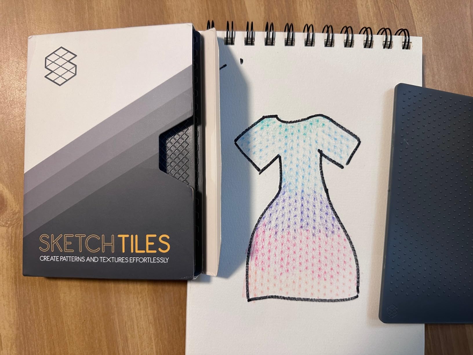 A dress drawing shaded with colored patterns beside SketchTiles and their packaging.